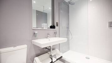 Een moderne badkamer met een douchecabine van glas, een witte wastafel en een toilet.