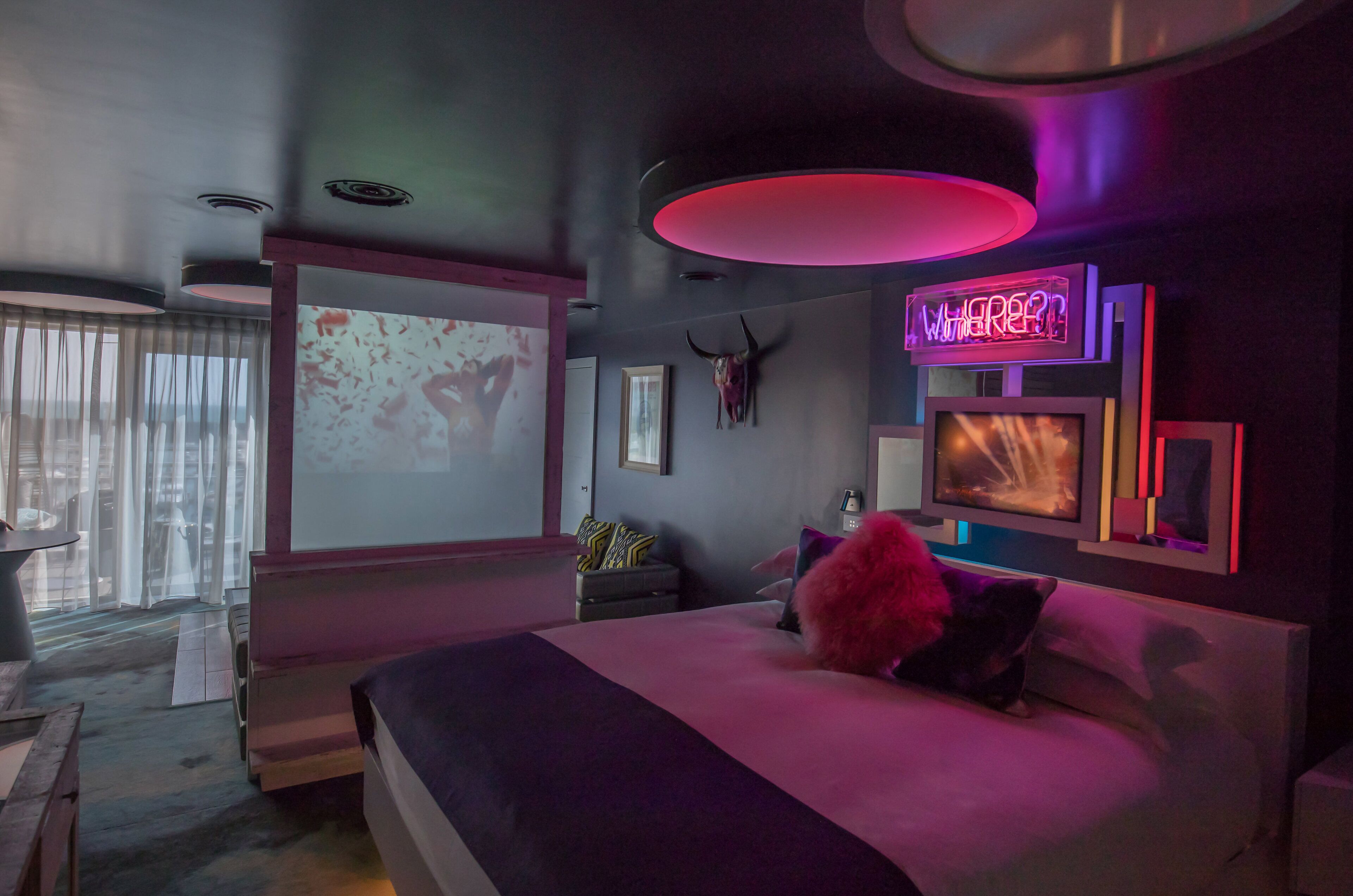 Een moderne slaapkamer met een groot bed, een wandgemonteerde televisie en een neonbord aan de muur.