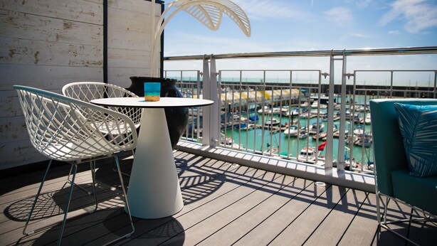 A balcony with a white metal chair, a table, and a view of a marina with boats. - Malmaison Brighton (Brighton)