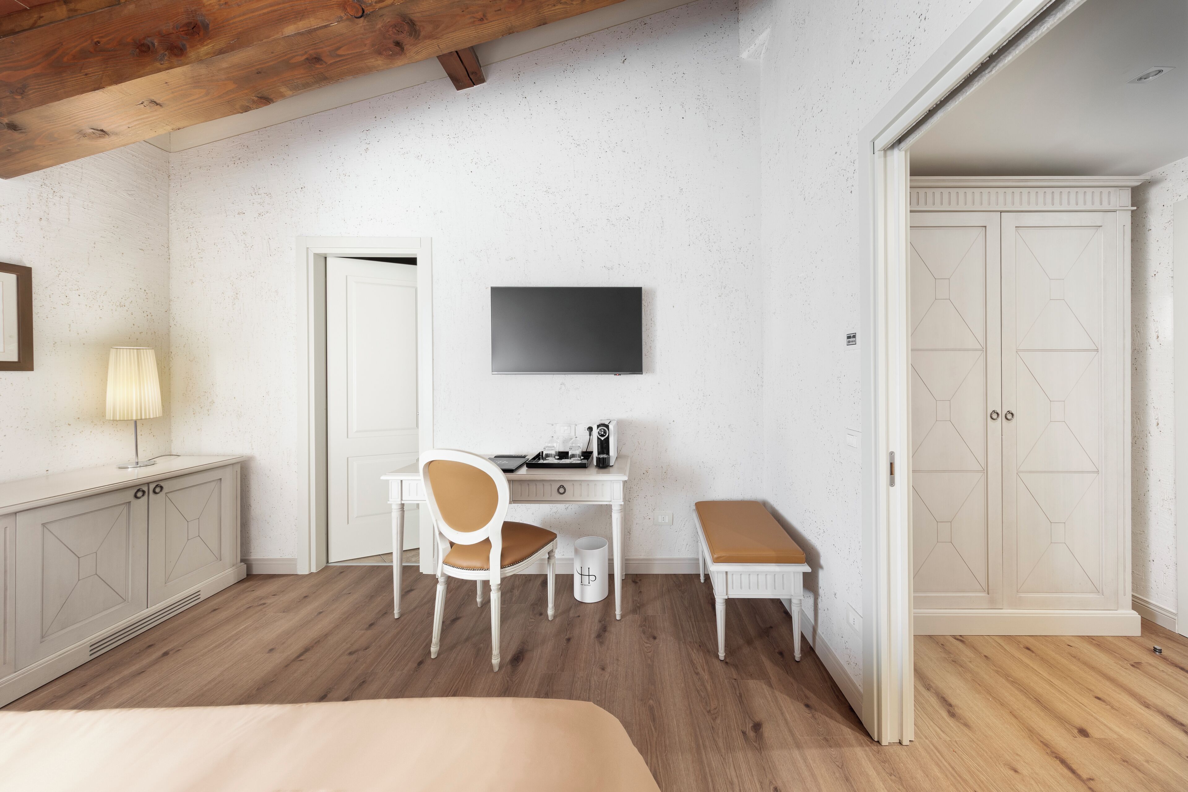 A bedroom with a bed, a desk with a chair, a TV, and a wardrobe.