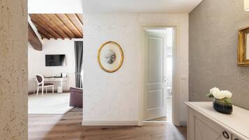 Un intérieur moderne avec un plancher en bois, un mur blanc orné d’un motif moucheté, un tableau encadré, un bureau avec une chaise et un meuble sur lequel est posé un vase de fleurs.