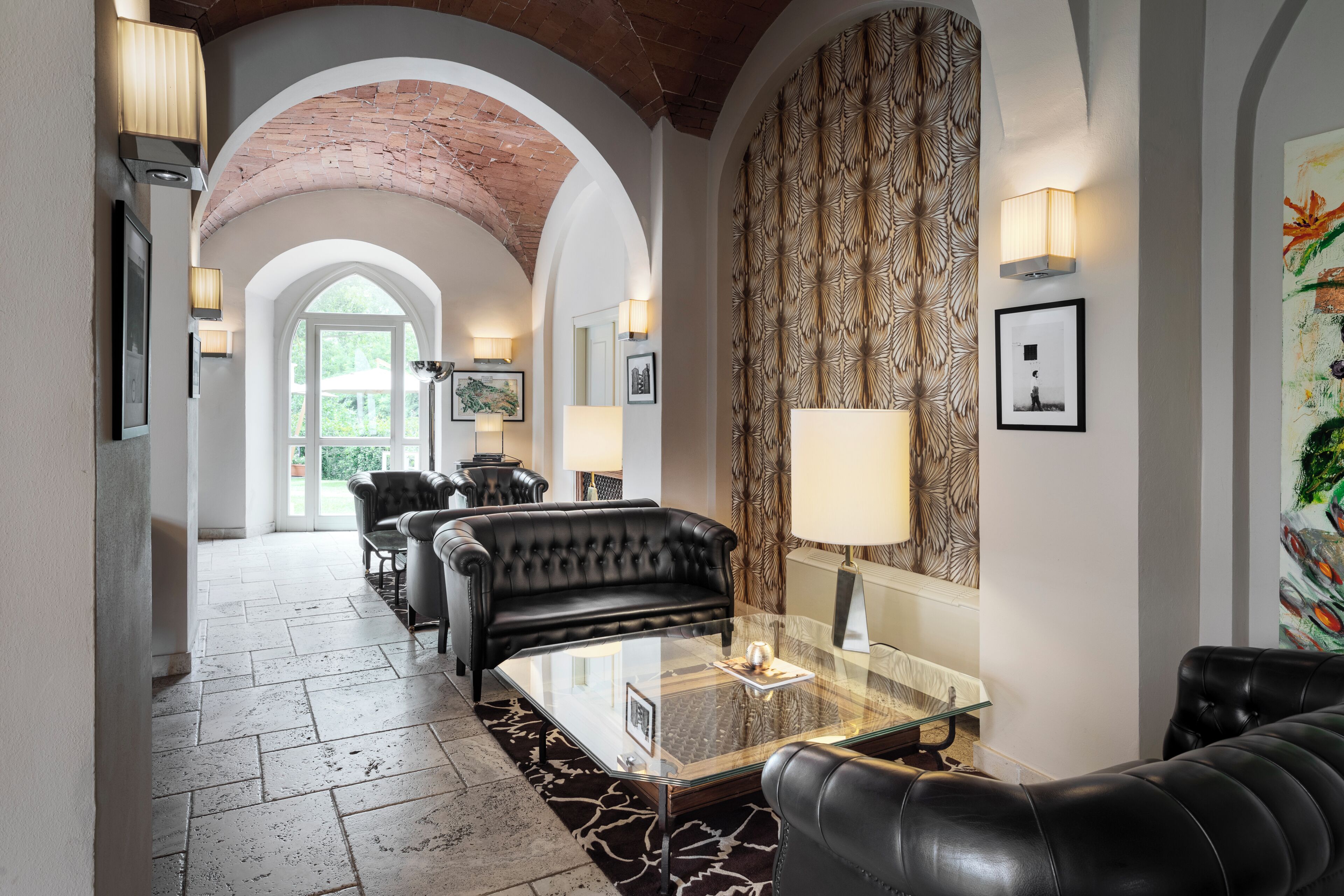 A hallway with a glass coffee table, black leather sofas, and wall-mounted lamps.