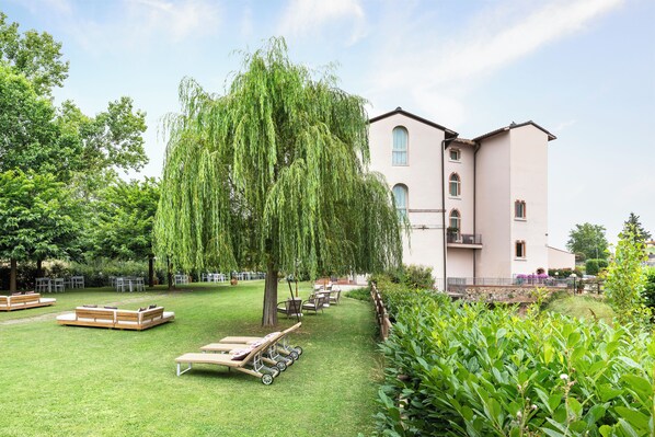 A garden with seating, a large tree, and a building with balconies. - LHP Certaldo Resort (Certaldo)