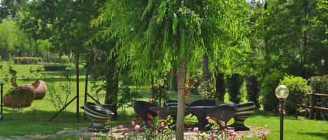 A garden with a weeping willow tree, a stone bench, and a flower bed with roses.