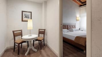 Een kamer met een bed, een ronde tafel met twee stoelen, een lamp en een ingelijst schilderij aan de muur.