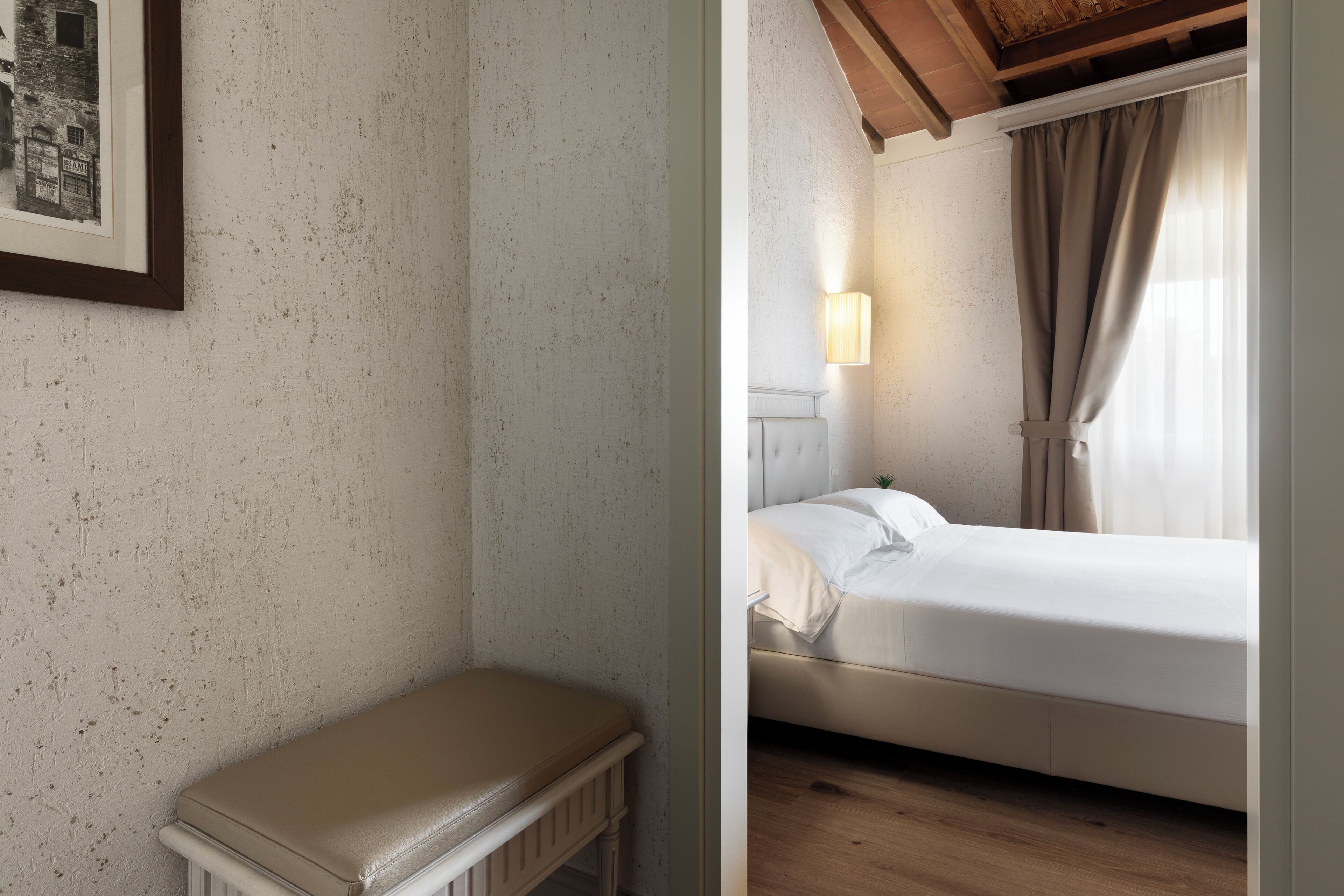 A bedroom with a bed, bedside lamp, and a small bench.