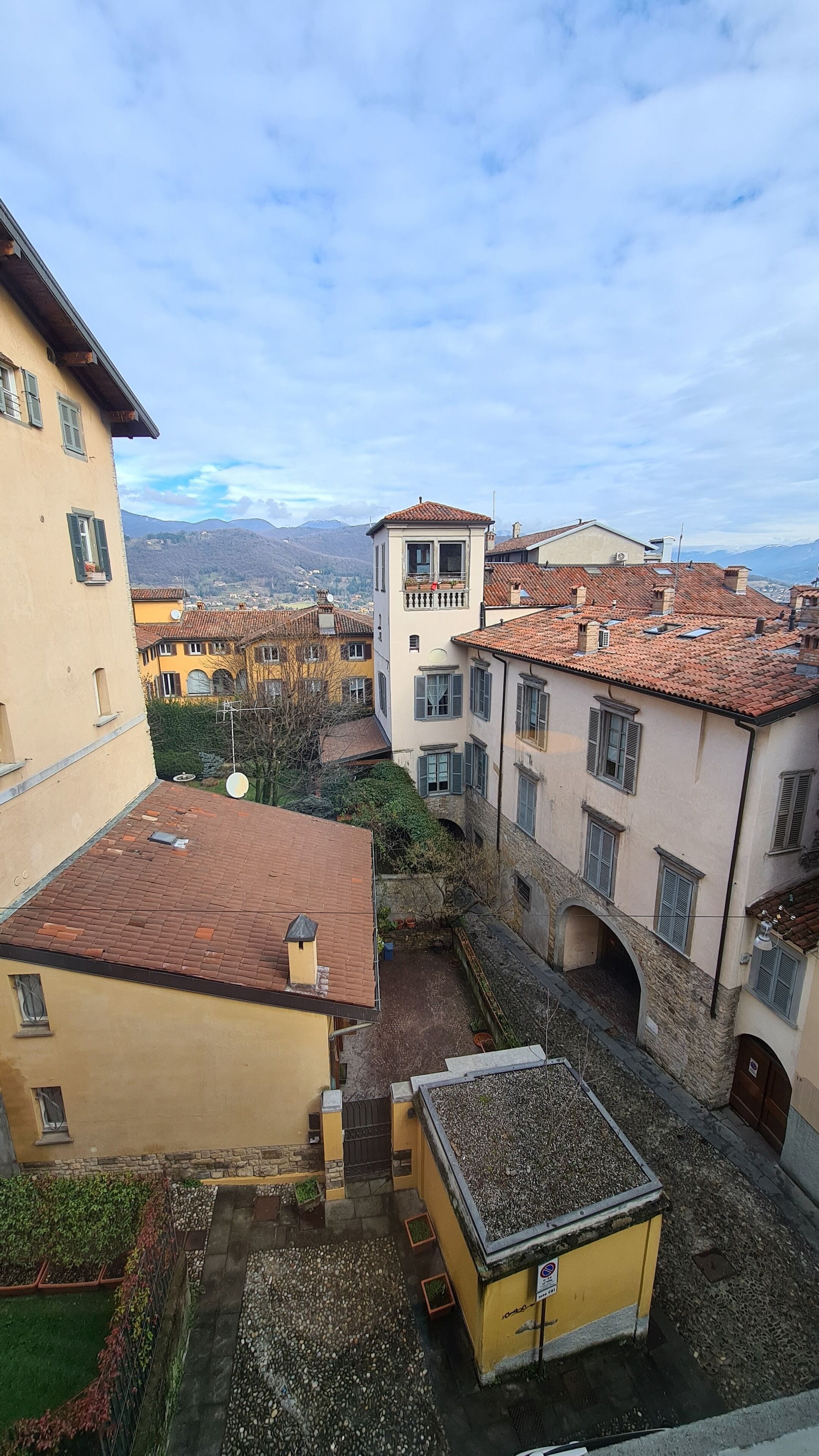 Um pátio com edifícios, uma pequena ponte e vista para montanhas ao longe.