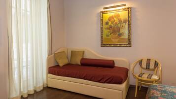 A room with a beige sofa, a wooden chair, a painting on the wall, and a sheer curtain.