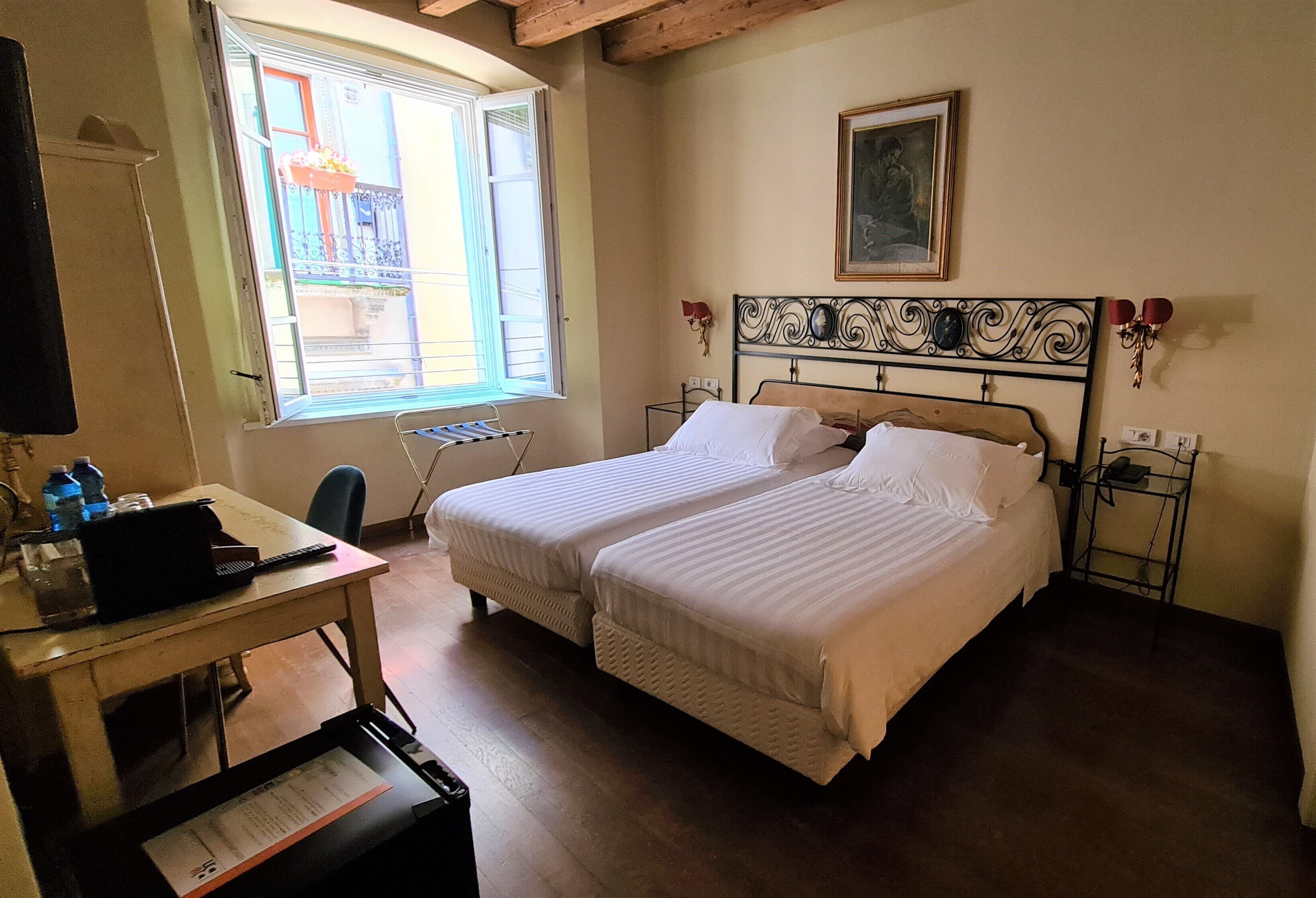 Habitación de hotel con dos camas, un escritorio con una computadora portátil, una silla y ventana con vista al exterior.