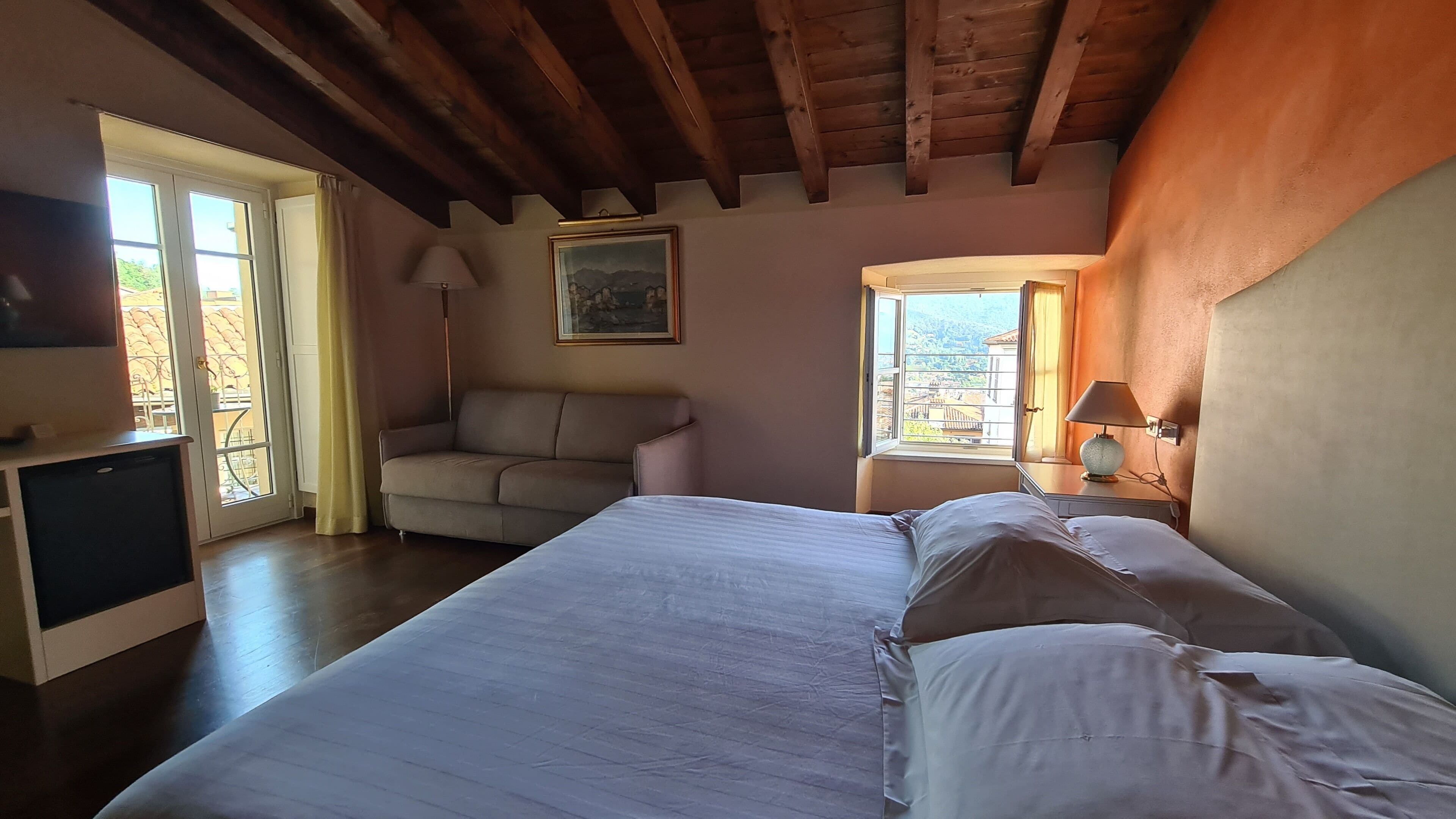 A bedroom with a bed, a sofa, a desk, a lamp, and a painting.