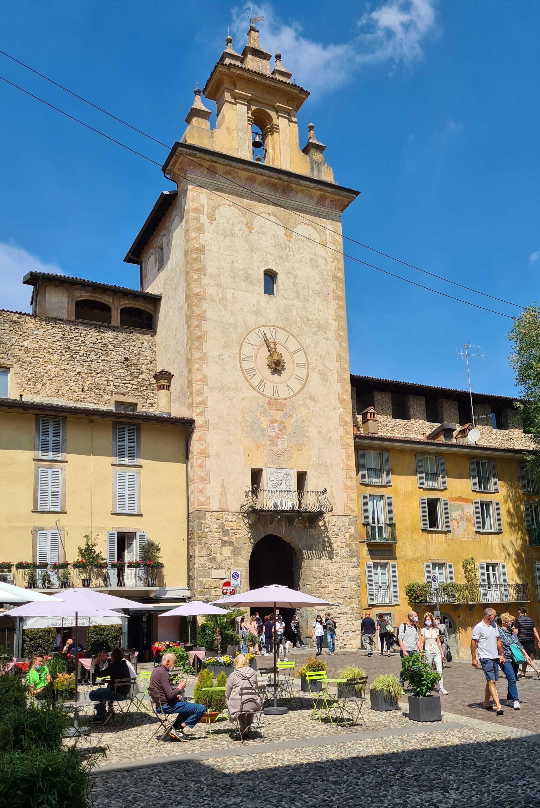 A historic building with a clock tower, outdoor seating, and a cobblestone plaza.