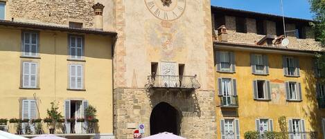 A historic building with a clock tower, outdoor seating, and a cobblestone plaza.