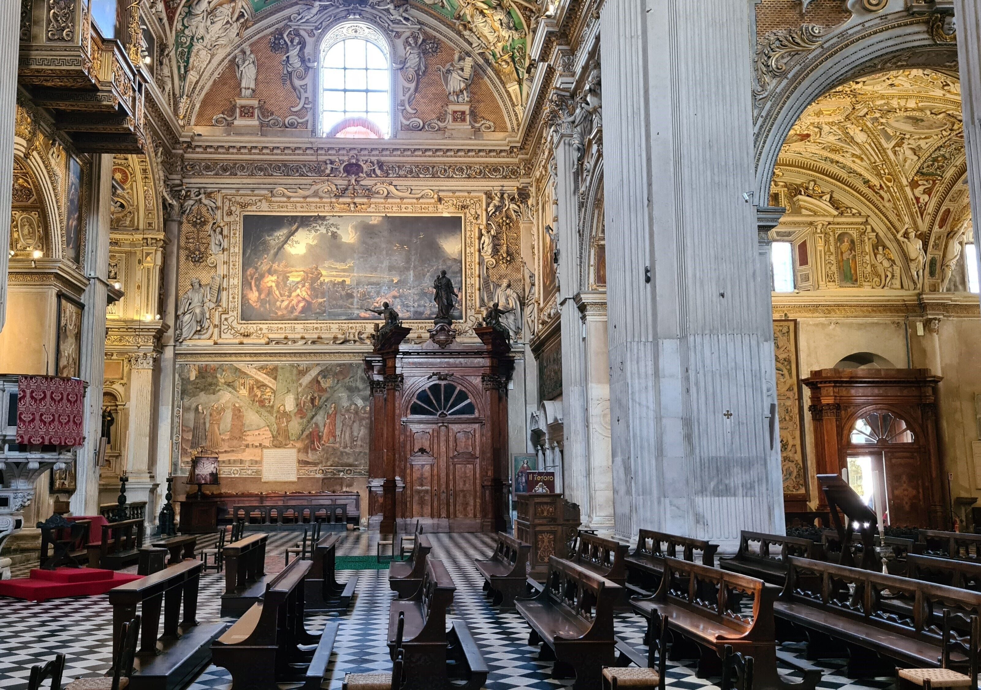 An ornate church interior with high ceilings, detailed frescoes, and a checkered floor.
