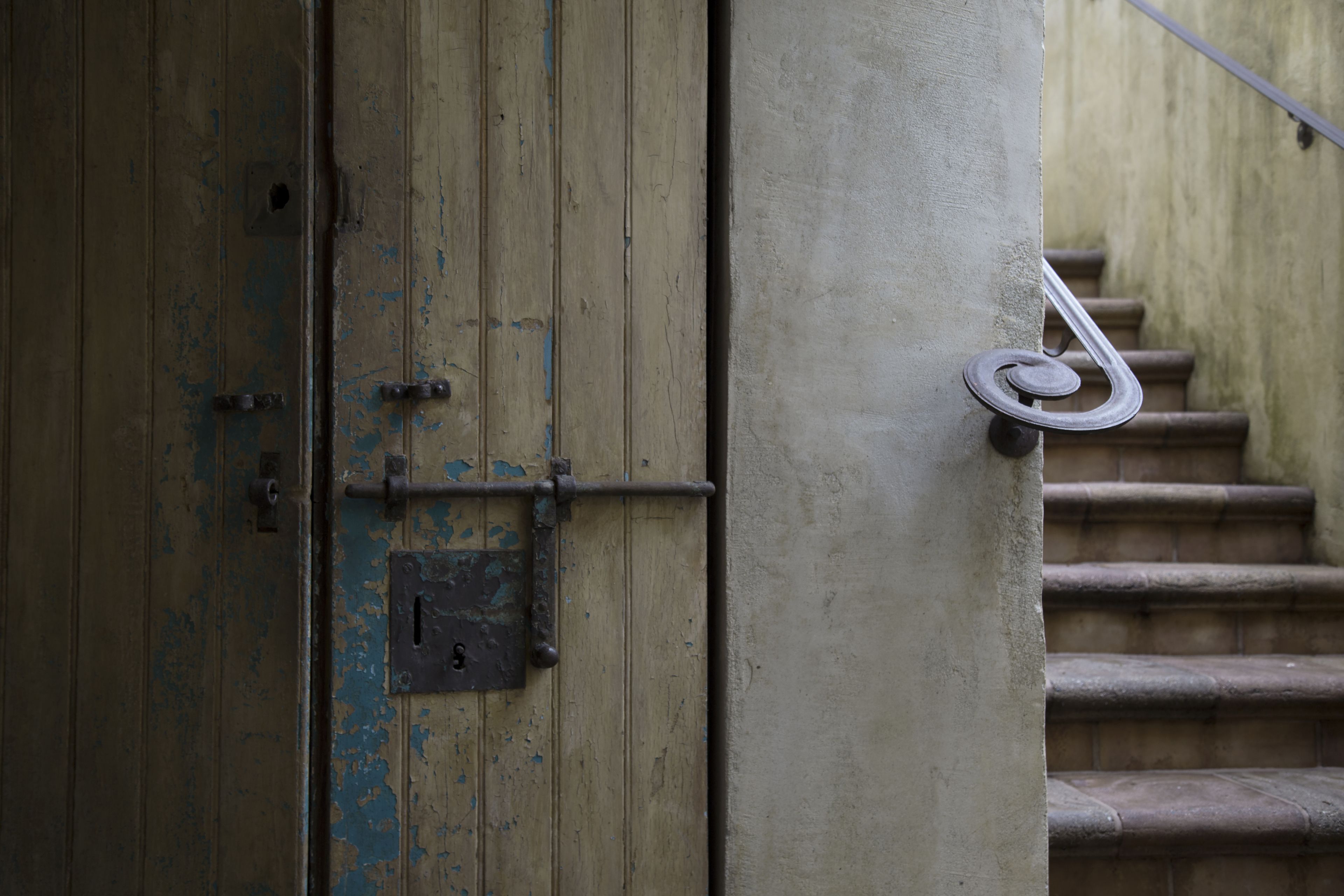 A weathered wooden door with a metal latch and a spiral staircase in the background.