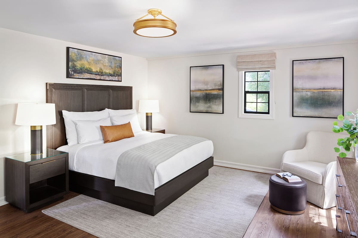 A modern bedroom with a large bed, bedside tables with lamps, a chair, and artwork on the walls.