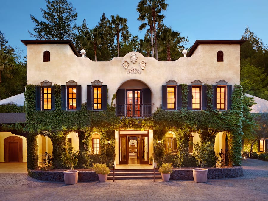 A large, stucco building with a central entrance, surrounded by lush greenery and potted plants.