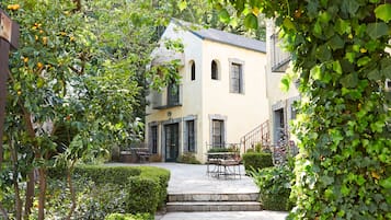 Eine steinerne Treppe führt zu einem Gebäude mit einem Balkon, umgeben von Grünpflanzen und einer Pergola.