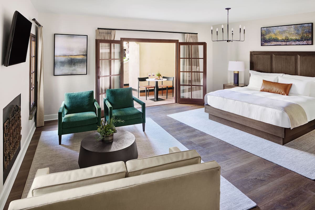 A hotel room with a bed, two chairs, a sofa, a coffee table, a TV, and a painting on the wall.