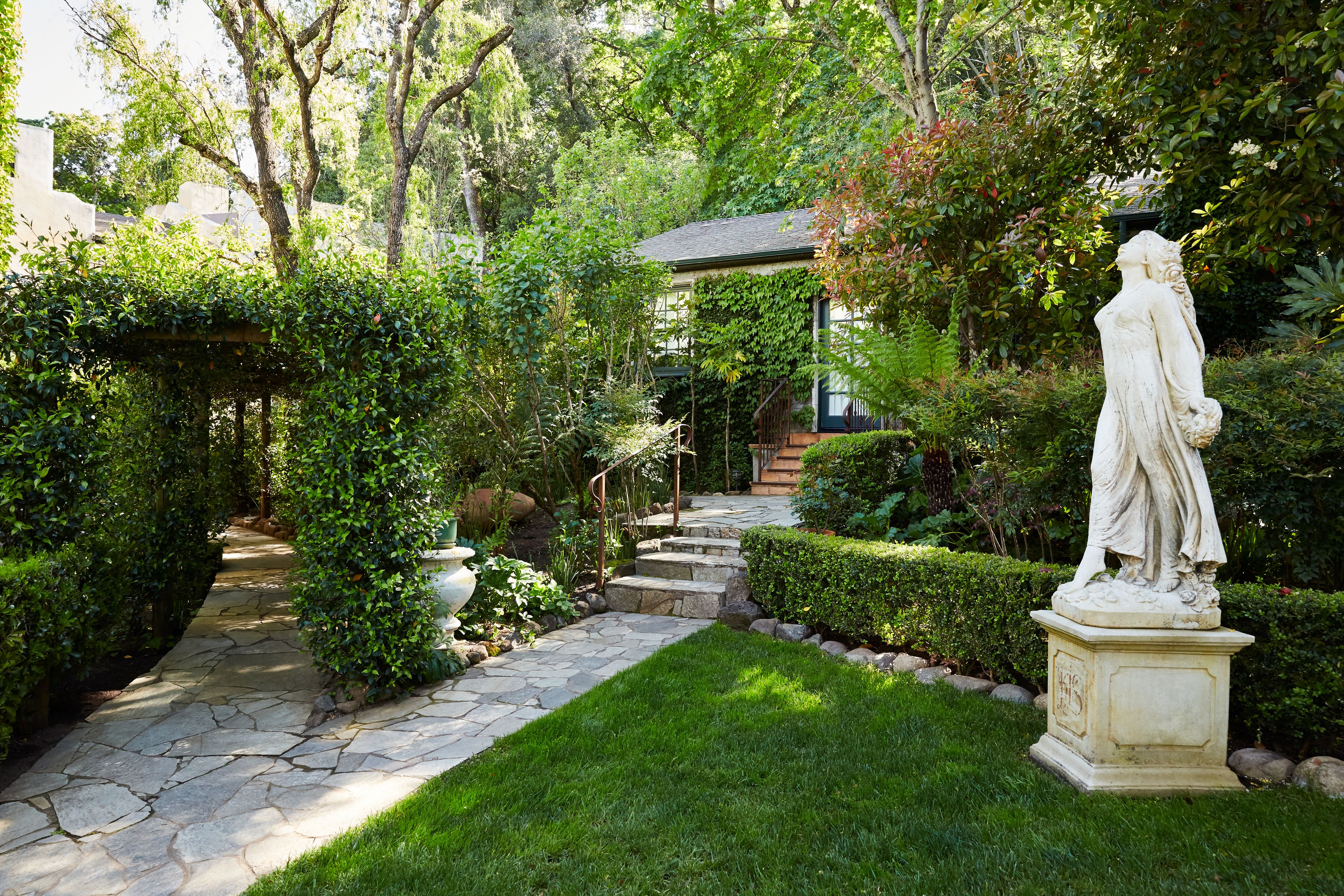A garden with a statue, stone pathway, and lush greenery.