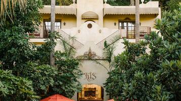 A courtyard with a central seating area, surrounded by lush greenery and a building with a distinctive architectural style.