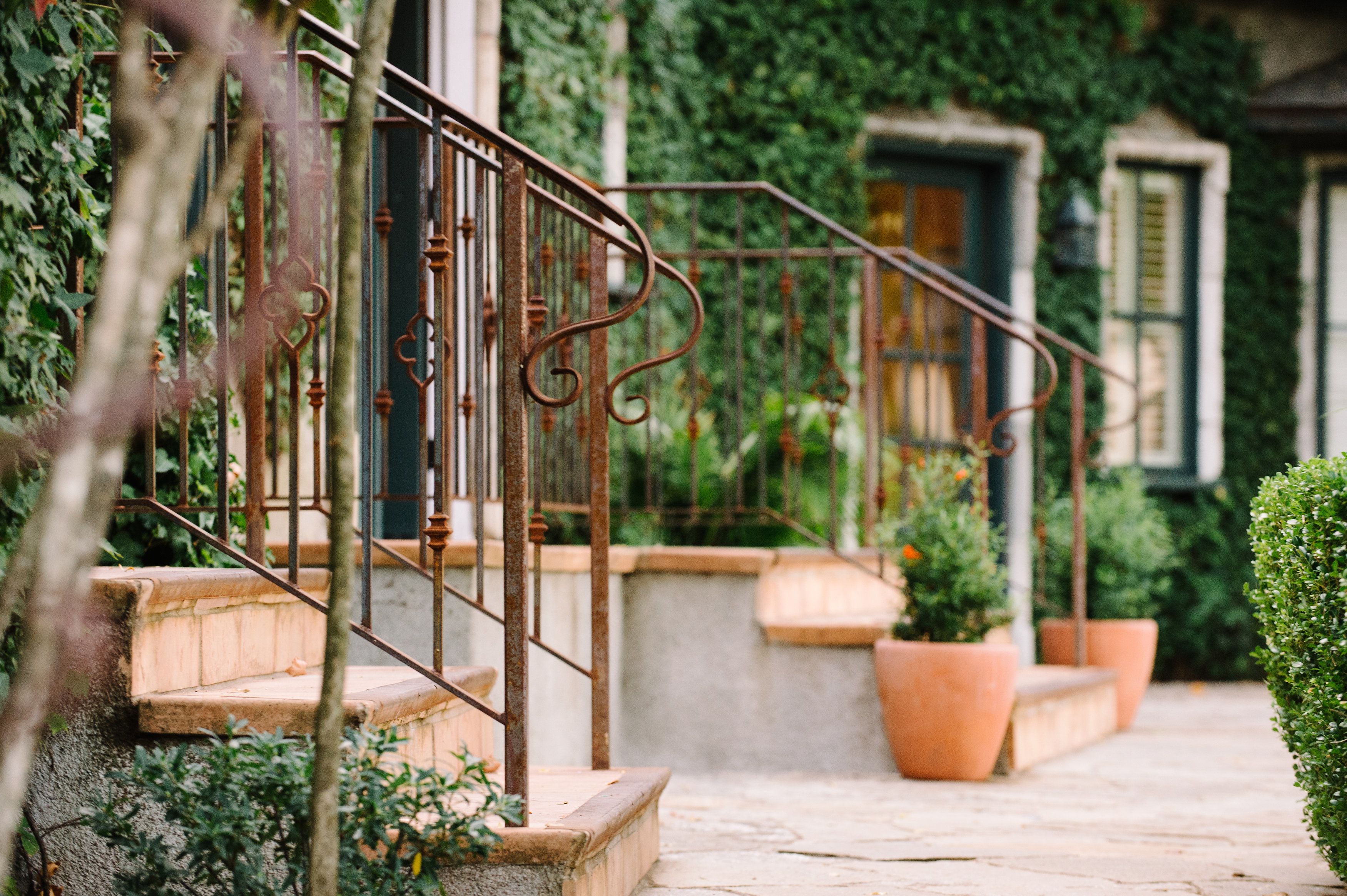 Un escalier en pierre avec des rampes métalliques mène à un bâtiment aux volets verts.