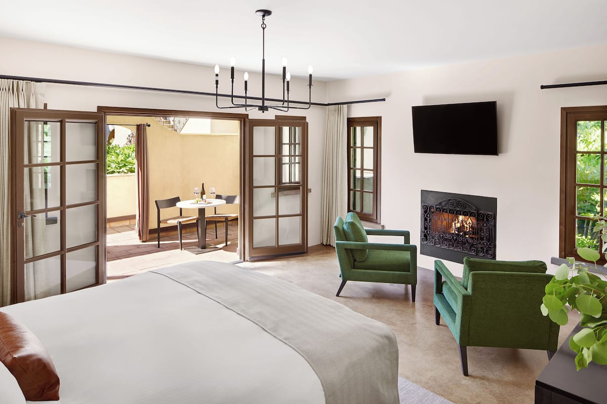 A hotel bedroom with a large bed, a fireplace, a TV, and a balcony with a table and chairs.