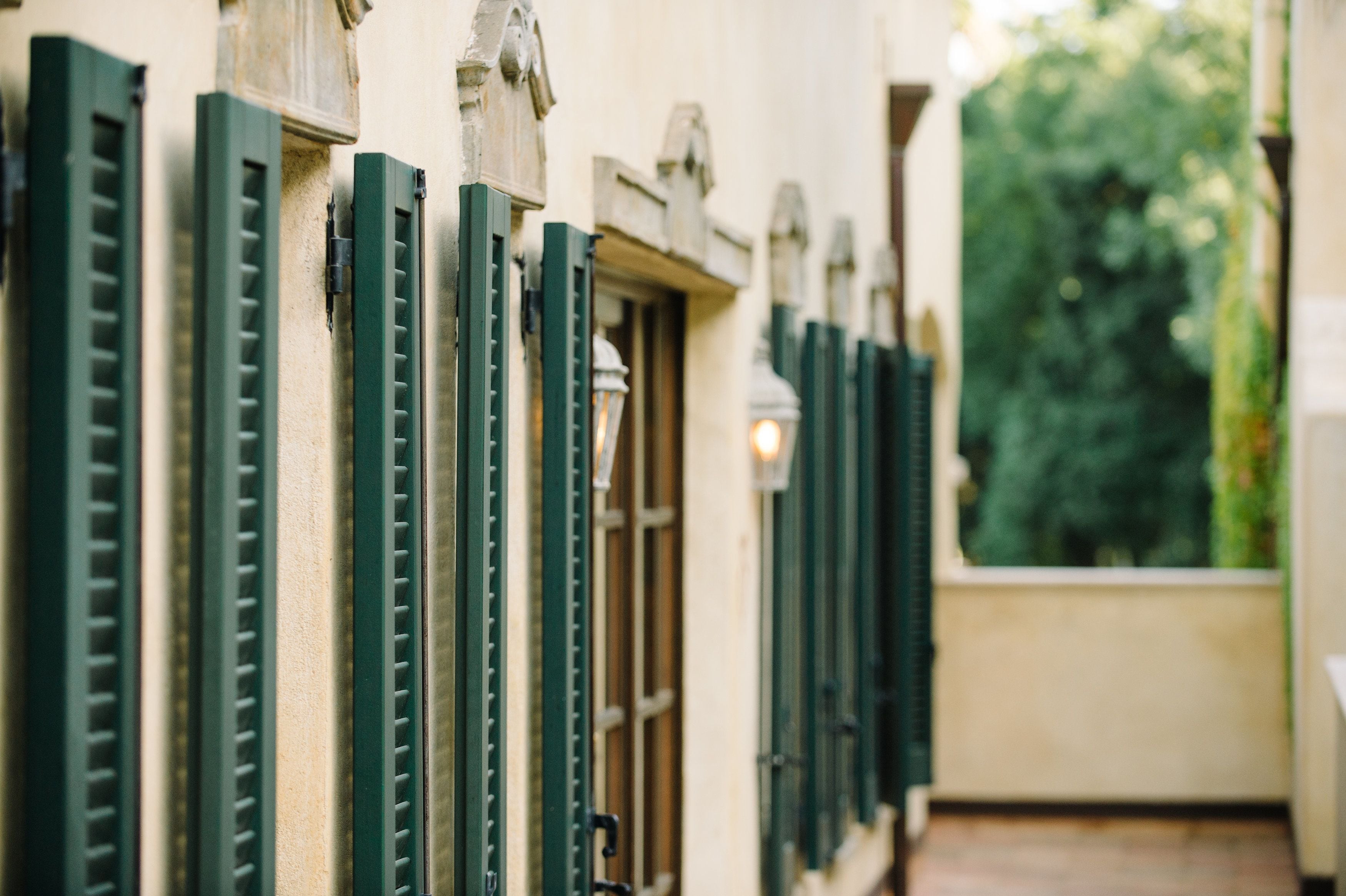 A row of windows with green shutters, a stone balustrade, and a view of greenery outside.