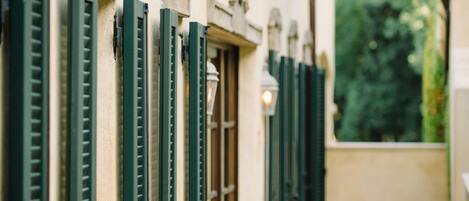 A row of windows with green shutters, a stone balustrade, and a view of greenery outside.