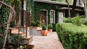 A stone pathway leading to a house with a metal staircase, surrounded by lush greenery and potted plants. - Kenwood Inn and Spa (Kenwood)