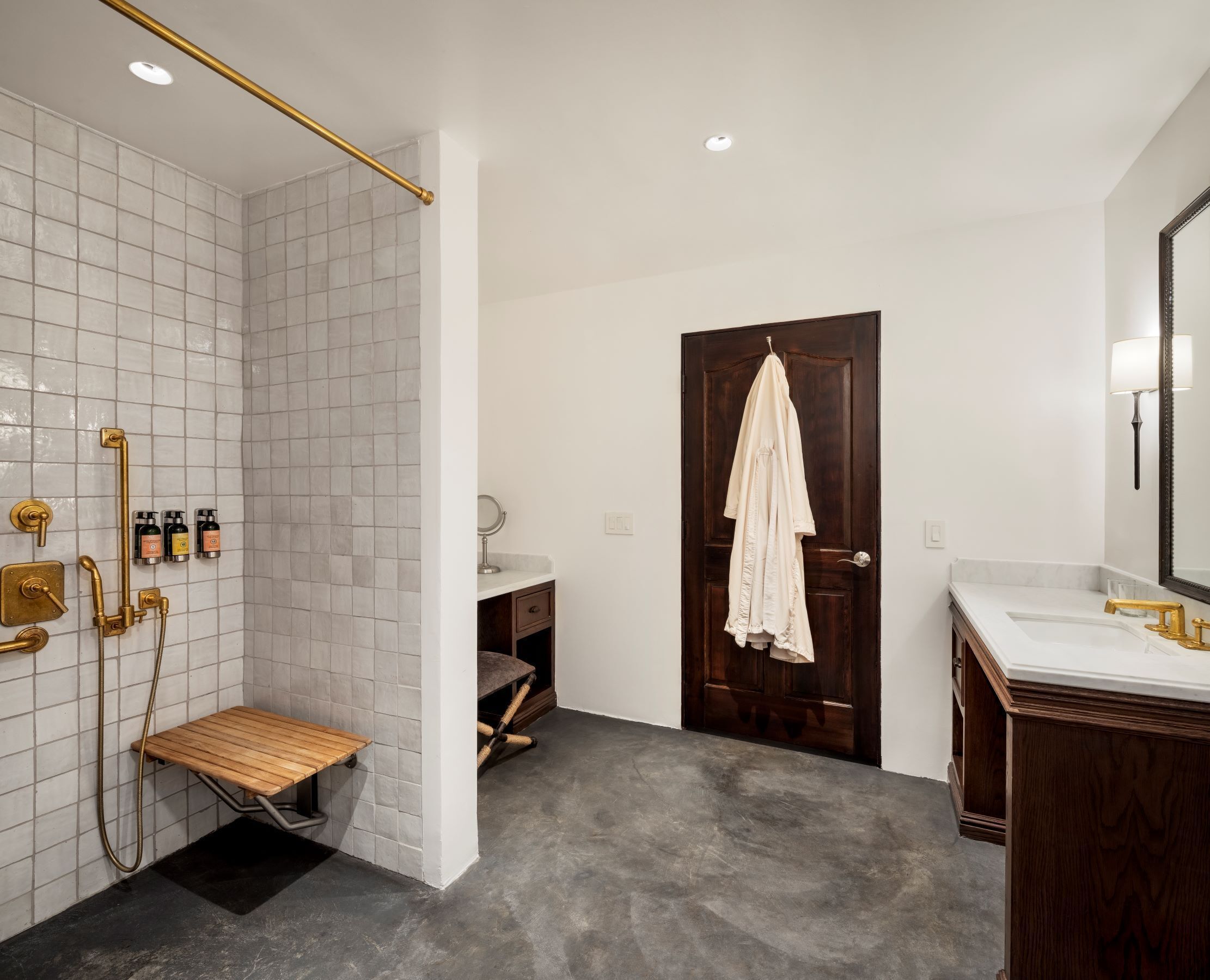 A modern bathroom with a shower, vanity, and a wooden bench.
