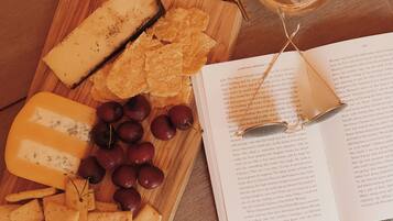 Una tabla de madera con diversos quesos, uvas y galletas, acompañada de un libro y una copa de vino.