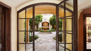An open arched doorway leading to a courtyard with a fountain, surrounded by greenery and a stone pathway. - Kenwood Inn and Spa (Kenwood)