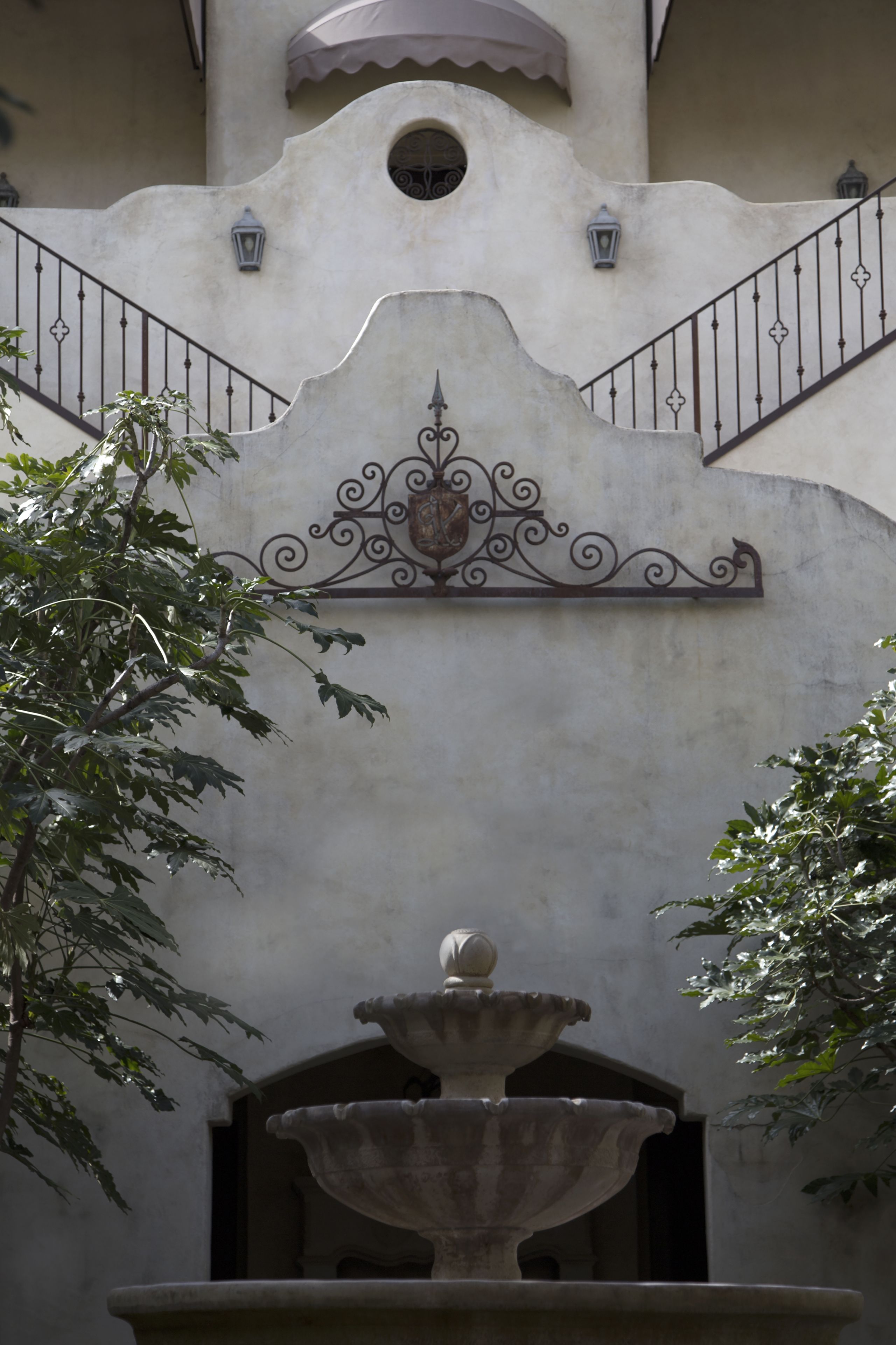 A stone fountain with a decorative metal railing in front of a building with a unique architectural design.