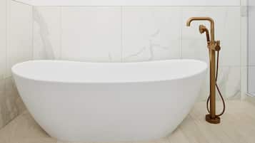 A freestanding bathtub with a gold faucet in a modern bathroom with marble walls and floor tiles.