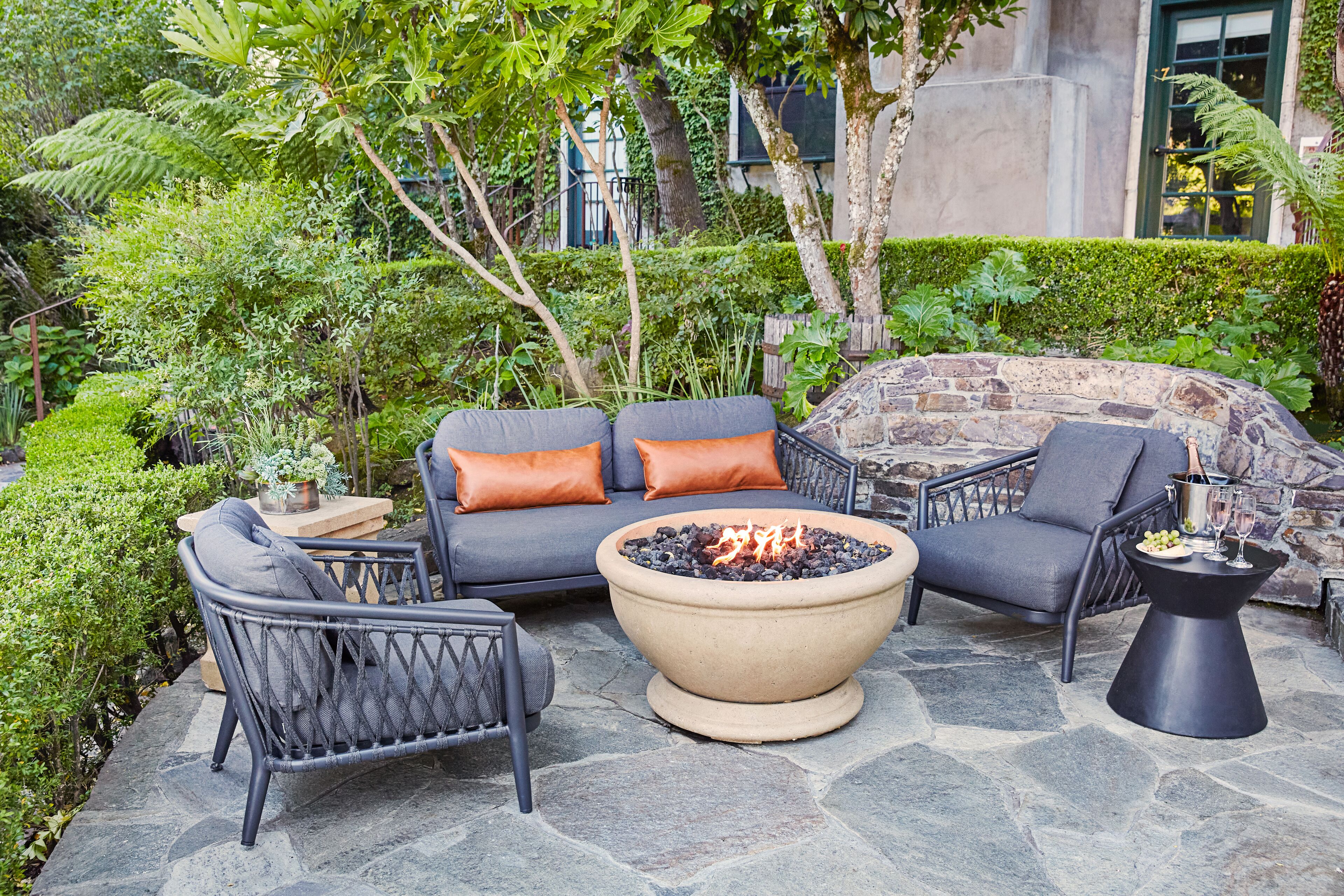 An outdoor seating area with a stone fire pit, cushioned chairs, and a table with a drink.