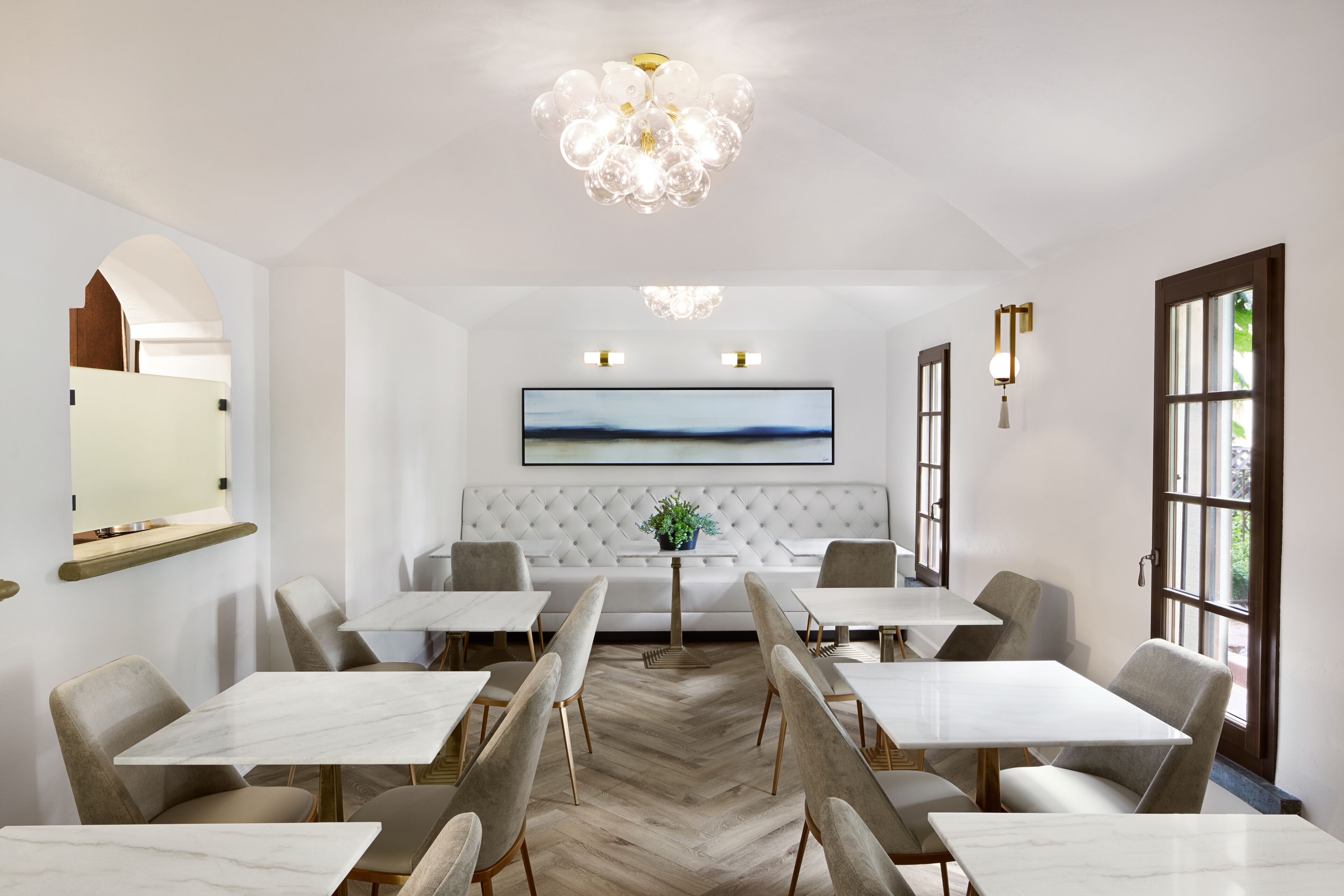 A modern dining area with white marble tables and chairs, a tufted sofa, and a chandelier.