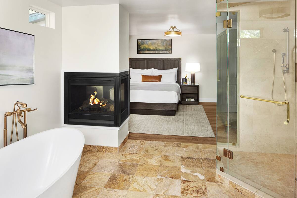 A modern bathroom with a freestanding bathtub, a glass-enclosed shower, and a fireplace.
