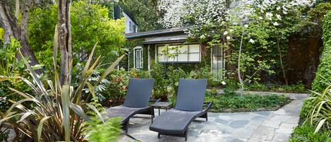 A garden with two lounge chairs, a stone pathway, and lush greenery.