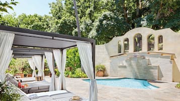 A private pool area with a covered seating area, stone flooring, and a fountain wall.