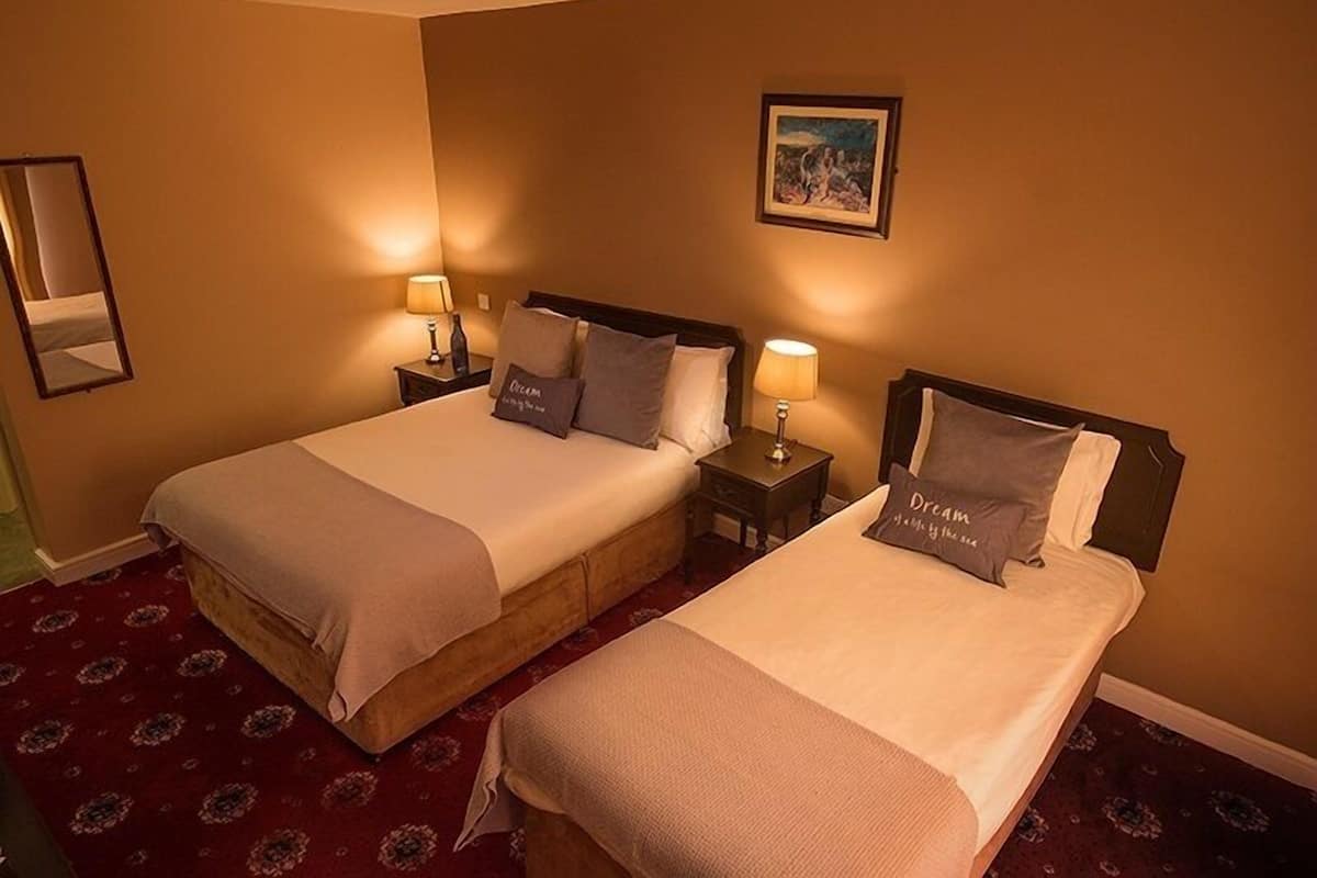 A hotel room with two beds, each with a nightstand and lamp, a framed picture on the wall, and a patterned carpet.