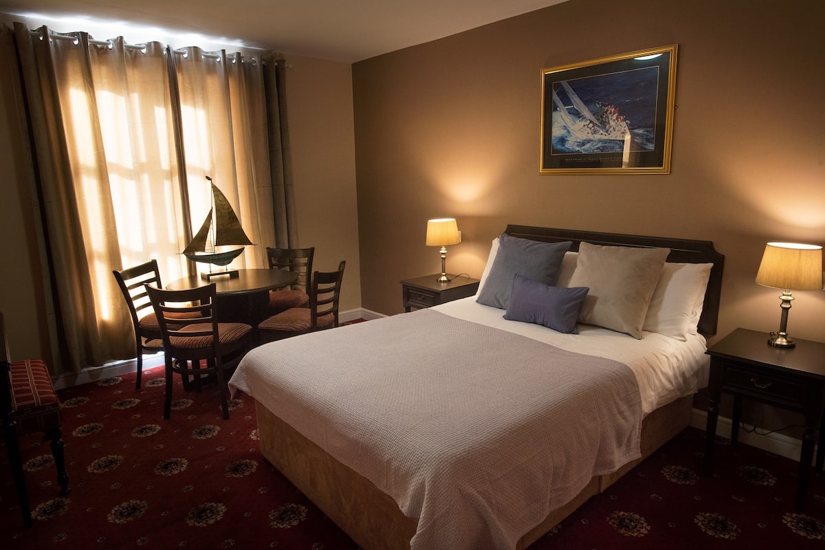 A hotel room with a large bed, a desk with a chair, two bedside lamps, and a framed picture on the wall.