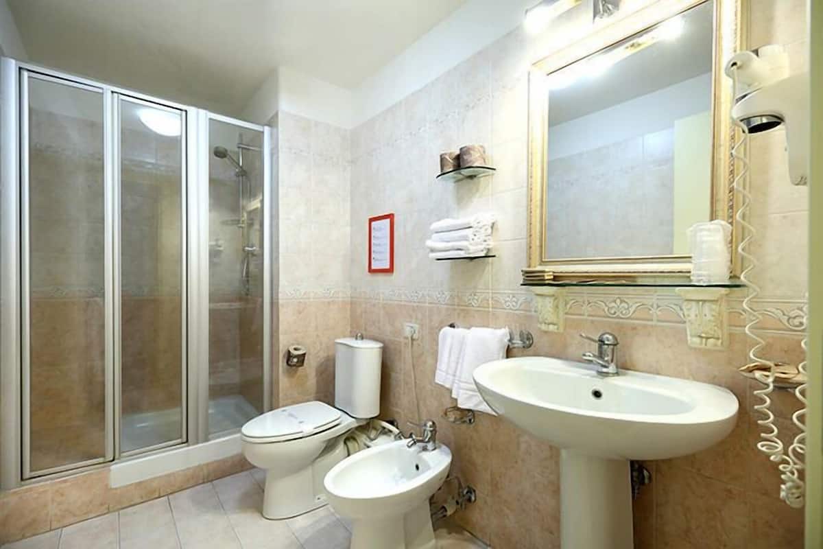 A bathroom with a glass-enclosed shower, a toilet, a bidet, and a sink with a large mirror.