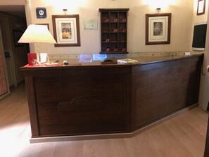 A reception desk with a dark wood finish, a lamp, framed certificates, and a small cabinet with red items. - Catania Centro Rooms (Catania)