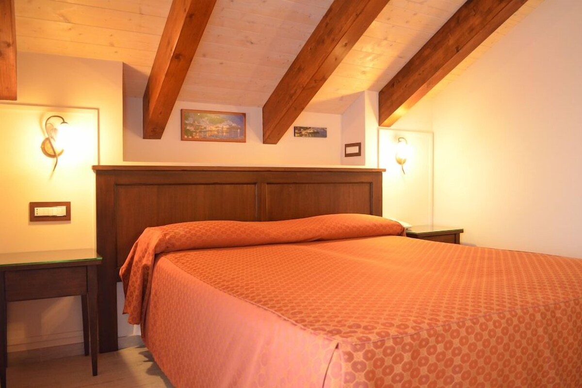 A bedroom with a wooden headboard, a bed with patterned bedding, bedside tables, and wall-mounted lamps.