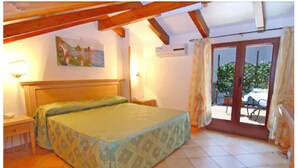 A bedroom with a bed, a nightstand, a painting on the wall, and a view through a glass door. - Hotel Due Torri (Agerola)