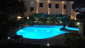 A swimming pool with a curved edge, surrounded by a stone wall and a low hedge. There are lounge chairs and a lifeguard stand visible. - Hotel Due Torri (Agerola)