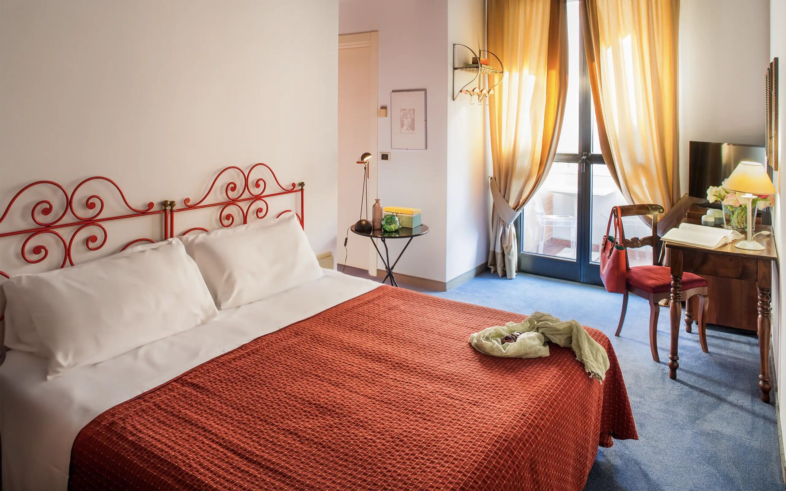 A hotel room with a bed, a desk, a chair, and a window with curtains.
