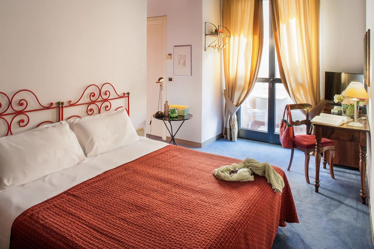 A hotel room with a bed, a desk, a chair, and a window with curtains.