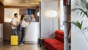 A reception area with a desk, a red sofa, and a plant. - Phi Hotel Palio (Asti)
