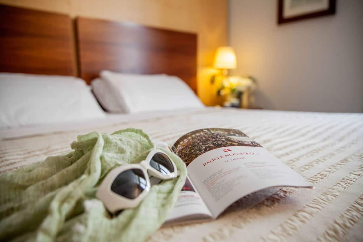 A neatly made bed with a book and sunglasses on it.